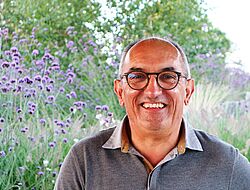 portrait d'un homme avec les cheveux gris, légèrement dégarni, vêtu d'un polo gris