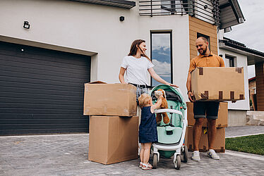 arrière-plan: maison moderne/ 1er plan: un homme, une femme et une petite fille avec des cartons de déménagement