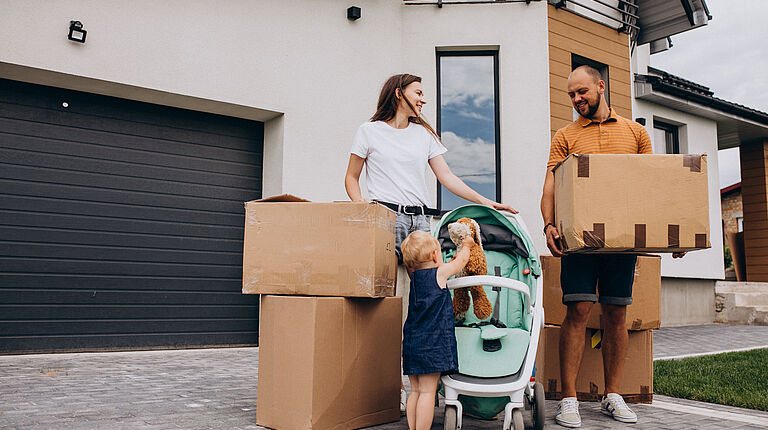 arrière-plan: maison moderne/ 1er plan: un homme, une femme et une petite fille avec des cartons de déménagement