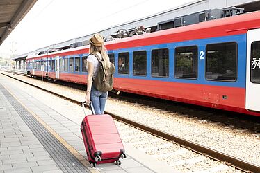 jeune femme de dos tirant une valise rouge sur le quai d'une gare