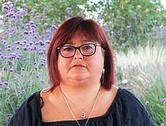 Femme avec cheveux mi-longs, auburn, lunettes avec contour noir, chemisier bleu foncé et collier avec chaine argenté - Agrandir l'image, .JPG 4,1 Mo (fenêtre modale)