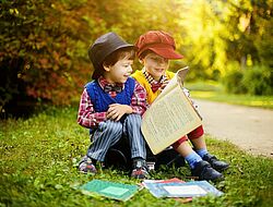 2 petits garçons assis sur un cartable et en train de lire